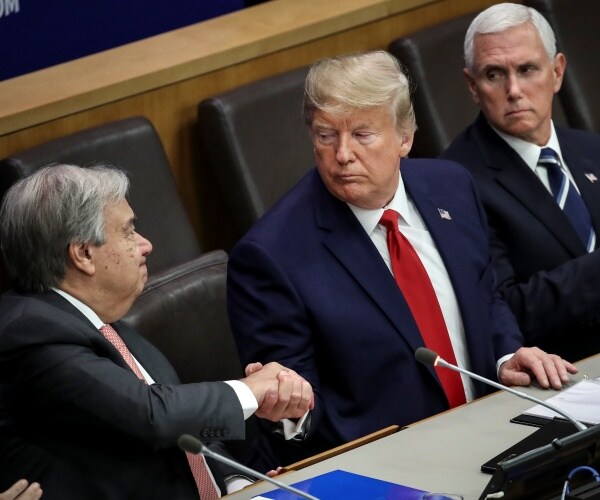 trump in a navy blue suit and red tie shakes hands with guterres and pence looks on sitting next to trump