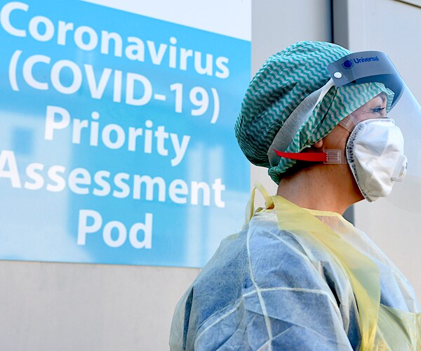 a nurse in pee pee eee walks past a covid-19 testing sign