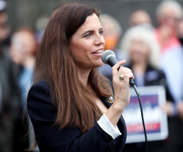 mace in a navy blue blazer speaking to a crowd holding a mic