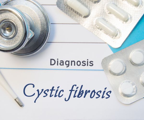 doctors stethoscope and two blisters of pills lying near pad with inscription of diagnosis cystic fibrosis