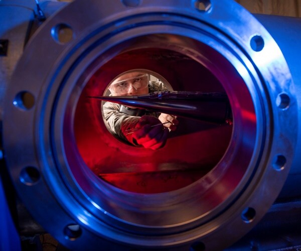 man wearing protective eye gear puts a tube into a chamber to measure the pressure and temperature inside it