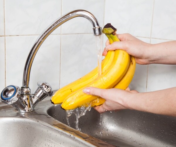 person washing bananas at sink