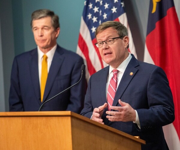 tim moore in a light red striped tie speaks as roy cooper in a yellow tie listens