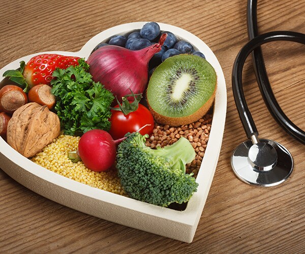 a heart-shaped wooden container filled with healthy food choices next to a stethoscope