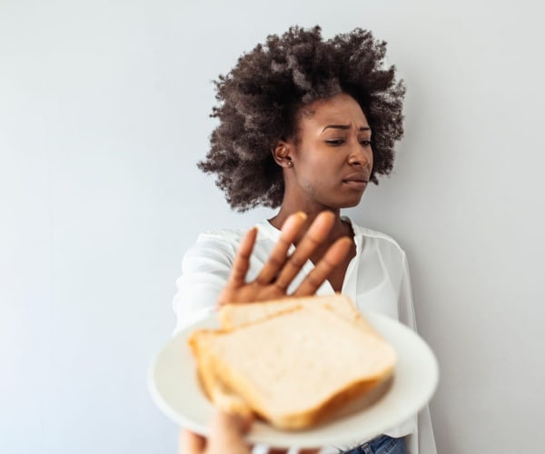 person with celiac disease with arm out saying 'no' to a piece of bread