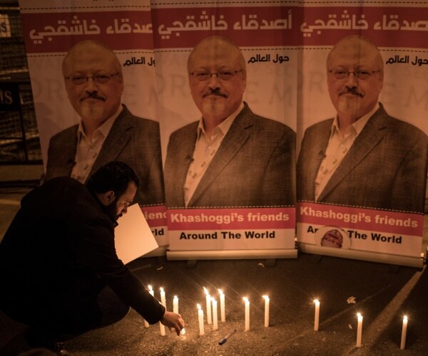 A man lights a candle in front of posters of Jamal Khashoggi during a candlelight vigil