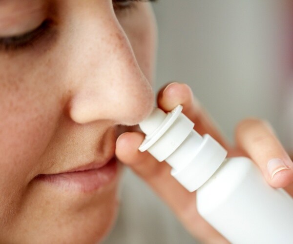 woman using a white bottle of nasal spray