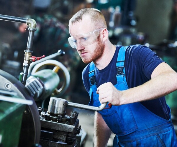 Worker turner operating lathe machine at industrial manufacturing factory