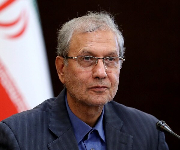 ali rebiei sits in front of iranian flag