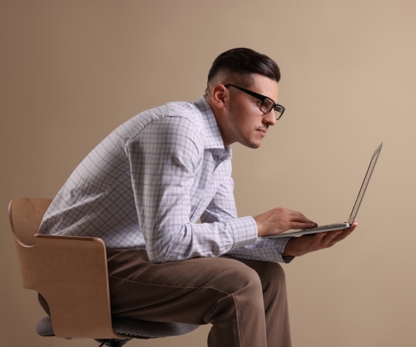 man sitting in chair slumped over using laptop on lap
