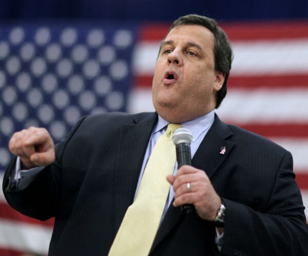 Former New Jersey Gov. Chris Christie is seen in a dress suit and tie with the us flag in the background
