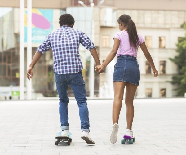 teenage boy and girl holding hands while riding skateboards