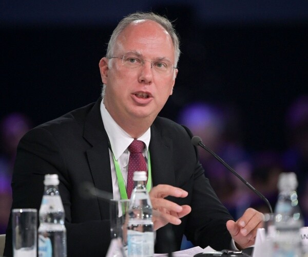 dmitriev in a black suit and burgundy tie speaking on a panel