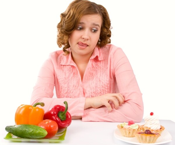 woman looking longingly at plate of pastries, not looking at plate of vegetables