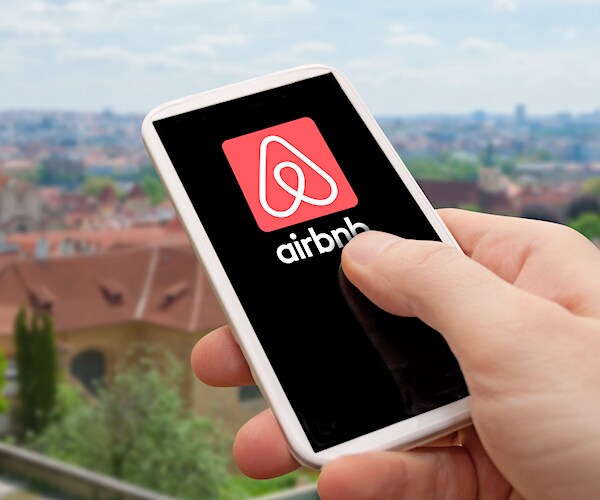 Photo of hand holding phone with Airbnb logo on the screen. Prague city in background