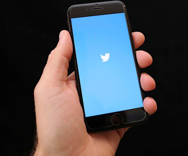 a man holds an iphone with a twitter icon on its screen as the application is opening