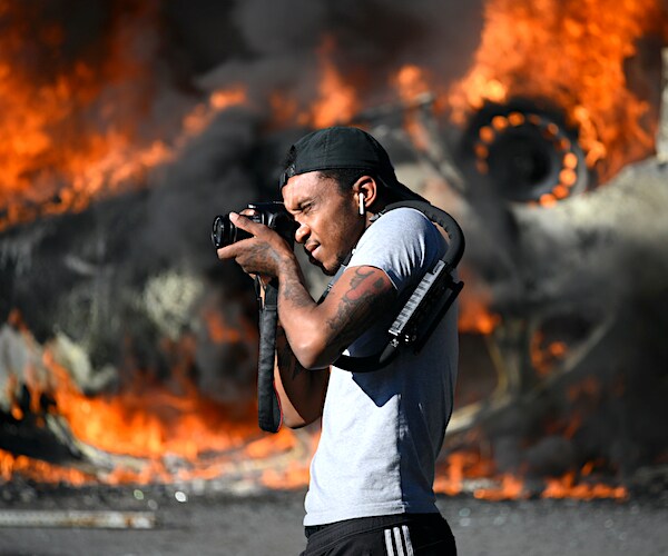 a man takes pictures in front of a raging inferno of an overturned police cruiser