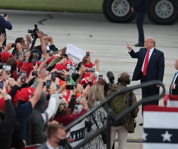 president trump stands on a tarmac facing a tightly packed crowd