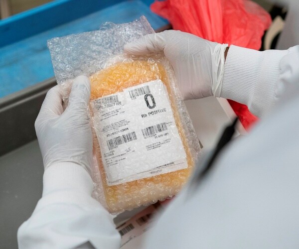 lab worker in a white coat and gloves handles packaged convalescent plasma in bubble wrap