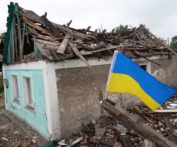 a ukrainian flag flies next to a damaged home