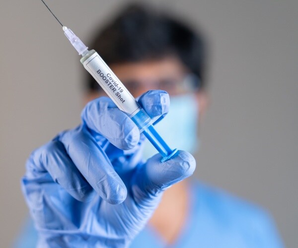 a healthcare provider holding a syringe labeled COVID-19 booster up close to the camera