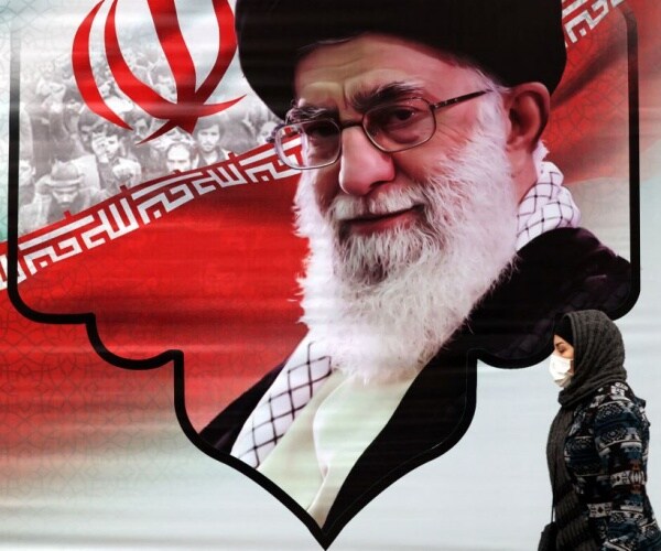iranian woman in head scarf walks past mural showing iran ayatollah ali khamenei