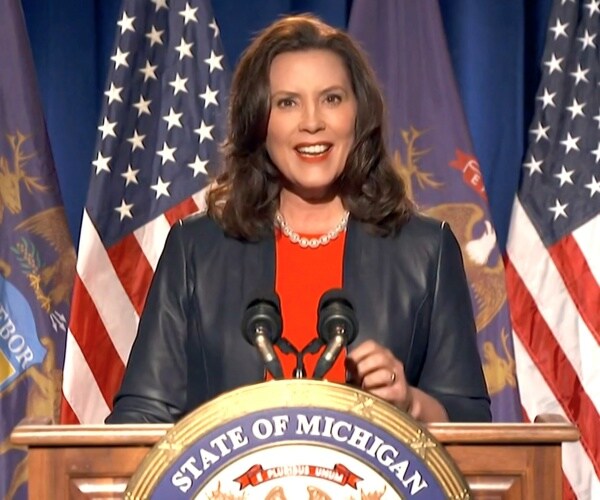 Whitmer speaking in a red  top and black jacket