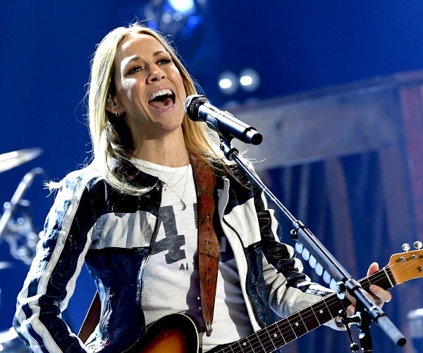 sheryl crow plays guitar and sings into mic onstage