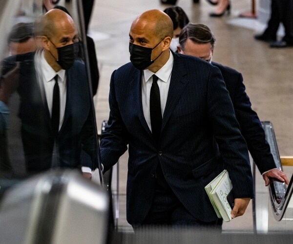 wearing a mask cory booker carries notepads and rides and escalator