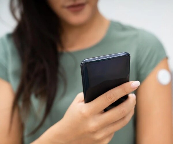 woman checking her glucose monitor results on smartphone