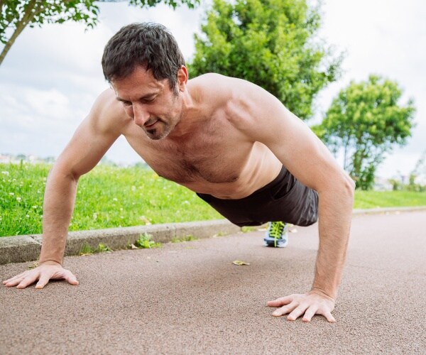 man doing pushups outdoors wearing black basketball shorts and sneakers
