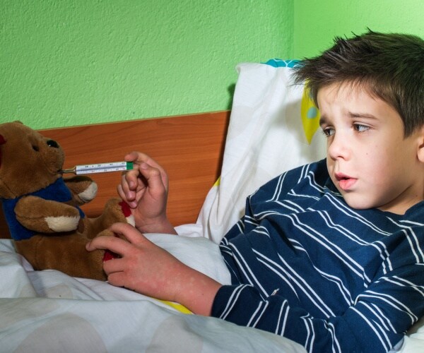 young boy in bed not feeling well, taking temperature of his teddy bear