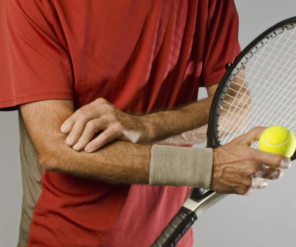 man holding tennis racquet rubs elbow in pain from tennis elbow 