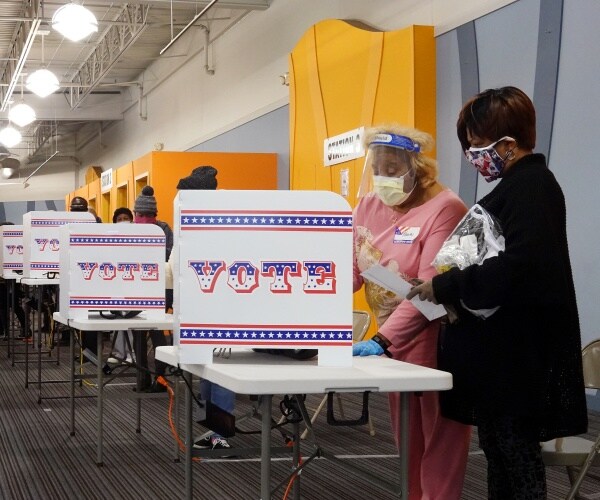 people wear masks to vote at tables with privacy folders