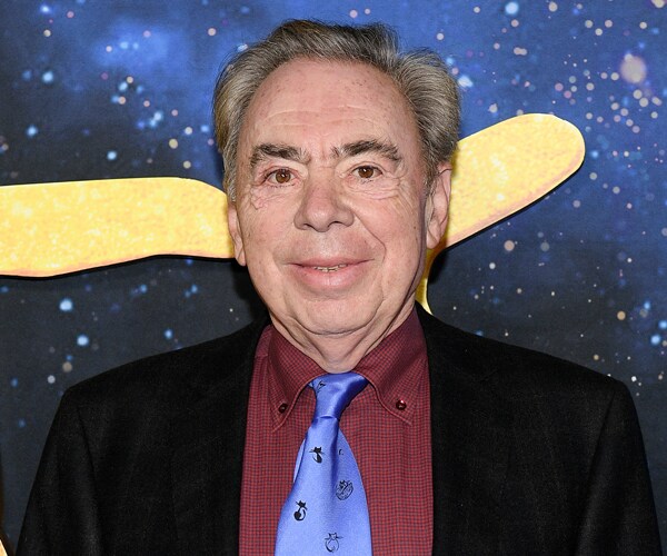 andrew lloyd webber smiling while wearing a dark-colored suit, red shirt, and blue tie