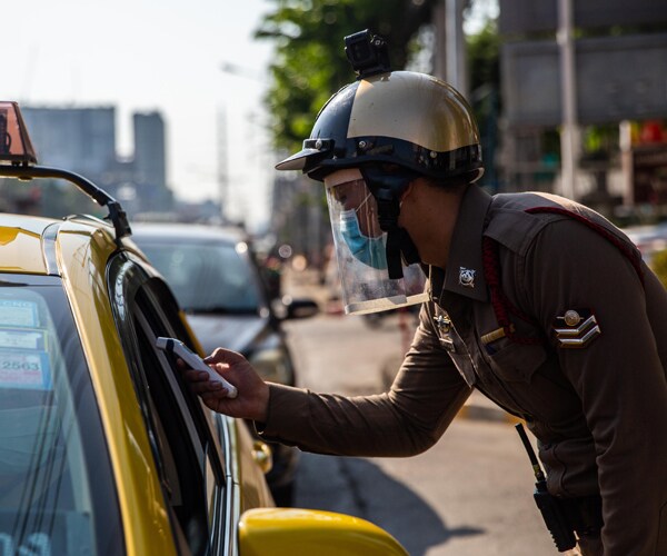 a member of thailand's military checks someone's temperature