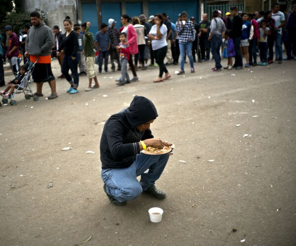 a migrant eats lunch as others line up for a meal outside the benito juarez sports center that is serving as a shelter 