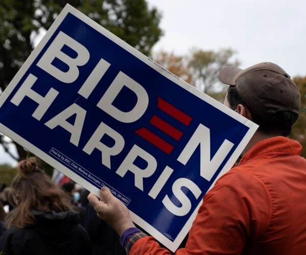 man in an orange coat carrying a biden harris sign