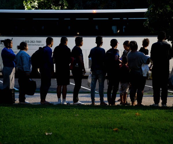 a line of migrants in front of a bus