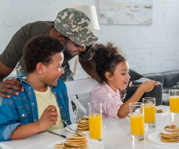 a sister and brother eating breakfast as Dad leans over the table talking to them