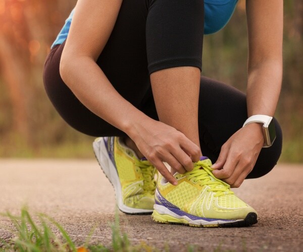 woman with apple watch on wrist bends down to tie shoe