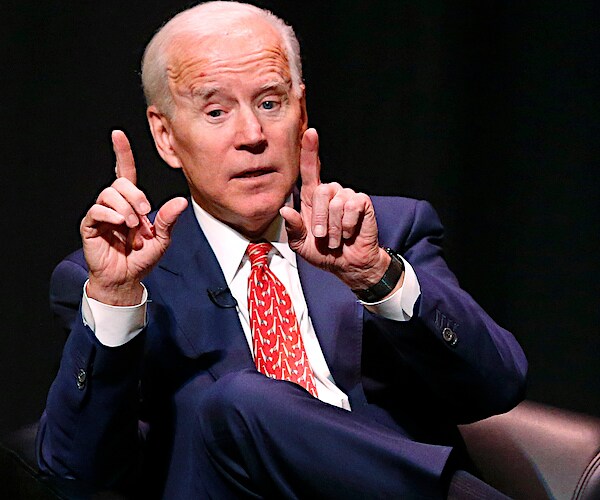 joe biden gestures with both hands while speaking on stage during a conference