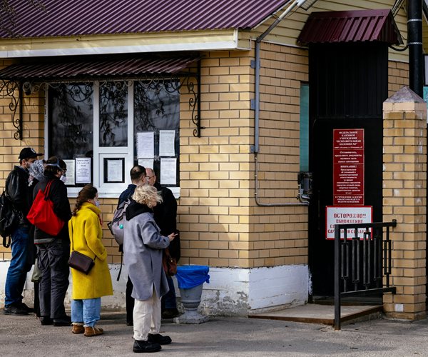 cluster of doctors with backs to the camera stand at the gate of a russian penal colony