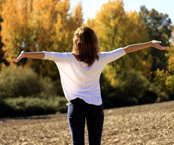 woman in field with arms up, breathing in the air