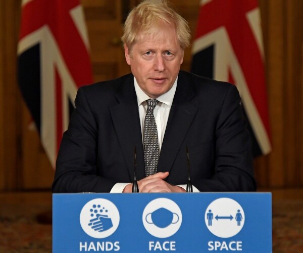 boris johnson's hands are clasped at a podium in front of the british flag.