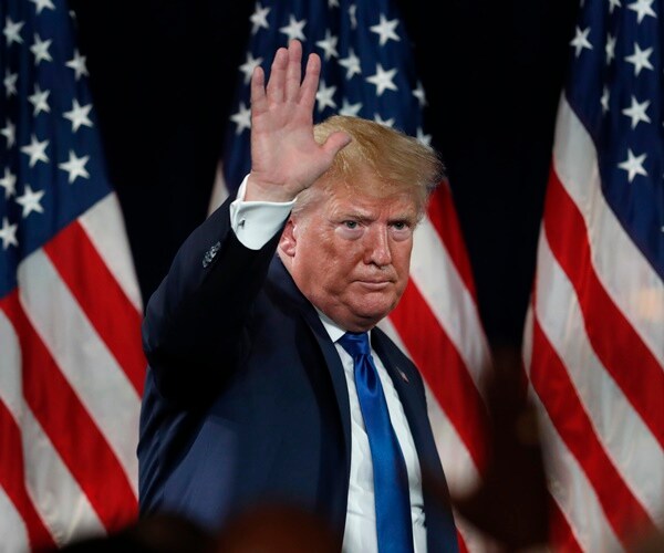 donald trump waves to supporters in front of flags