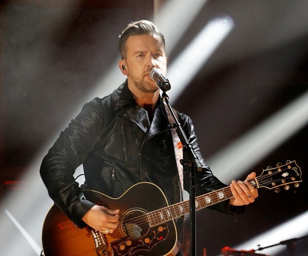 tj osborne plays guitar and sings into mic onstage