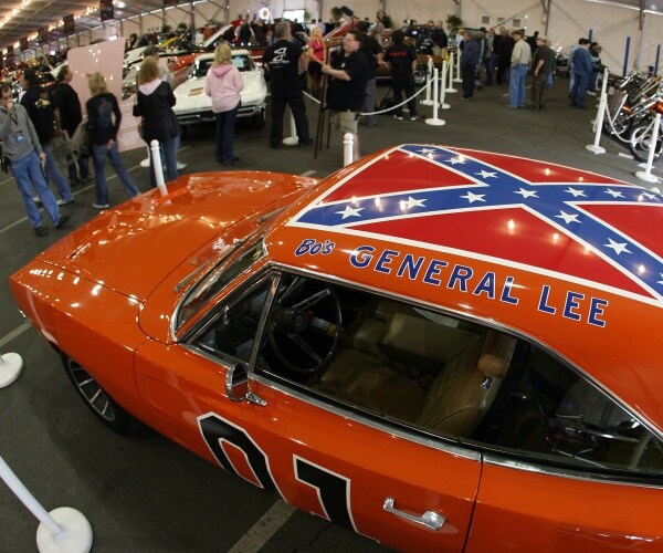 orange dodge charger with confederate flag on the roof of the car sits at an auction