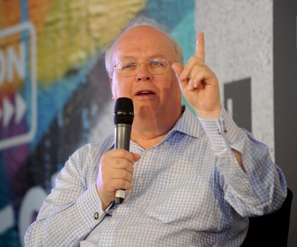 karl rove in a blue and white checkered print shirt speaking into a mic on stage