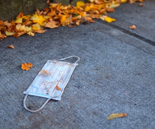 surgical mask lying on a sidewalk by autumn leaves